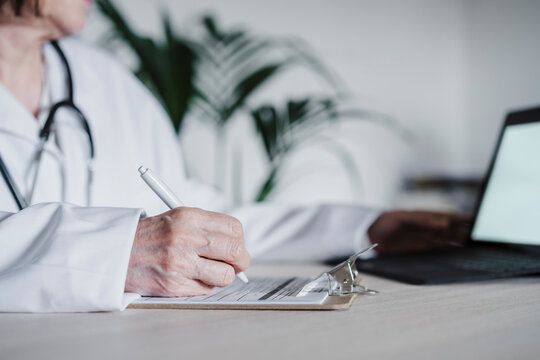 Hand of female doctor preparing report on clipboard at desk in hospital