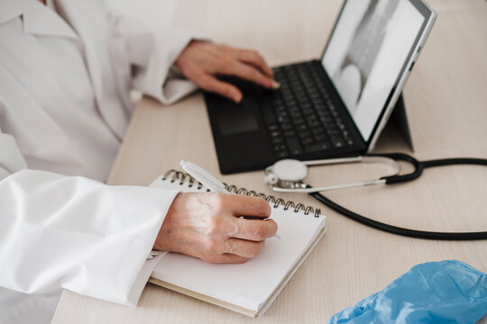 Female doctor using digital tablet while writing in diary at desk in medical clinic