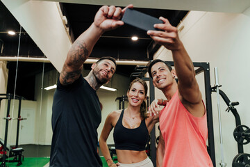 Smiling friends taking selfie through mobile phone at gym