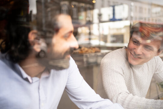 Male coworkers discussing in coworking office during coffee break seen through glass