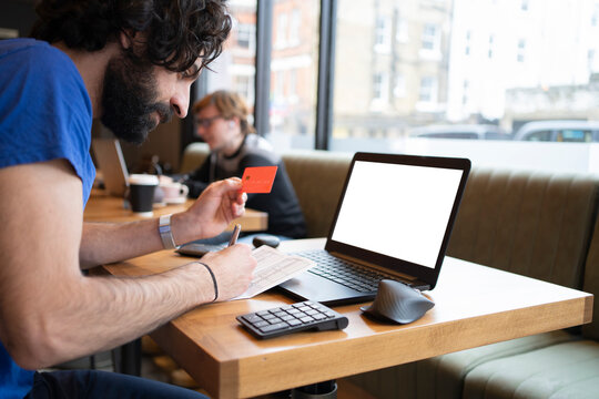 Male entrepreneur holding credit while making online payment on laptop at office