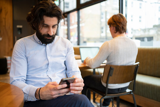 Businessman Using Smart Phone While Colleague Working On Laptop At Coworking Office