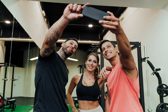 Smiling friends taking selfie through mobile phone at gym