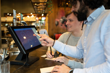 Male entrepreneur explaining table setup to colleague on restaurant computer