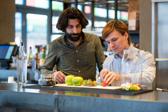 Bartender looking at trainee cutting strawberry at bar counter