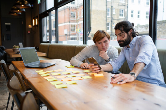 Male coworkers looking at smart phone while planning strategy at office