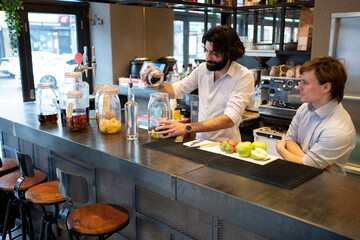Trainee looking at male bartender putting fruits in jar at bar counter