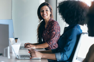Smiling female professional looking at colleague while working on laptop in office