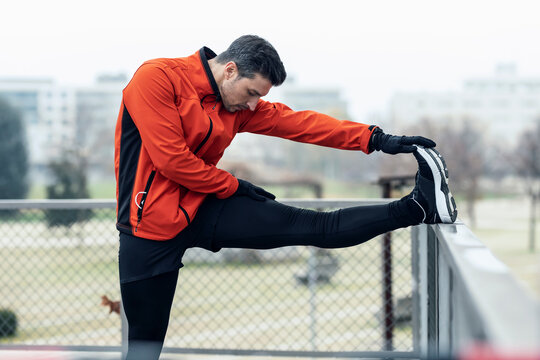 Male athlete touching toe while leg on chainlink fence at park