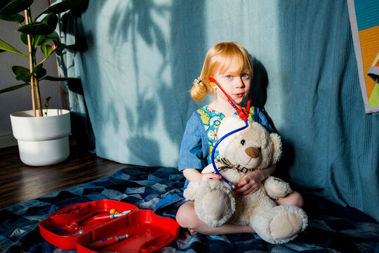 Aspiring blond girl playing with stethoscope and teddy bear at home