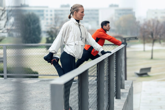Male and female athletes doing stretching exercise by chainlink fence at public park