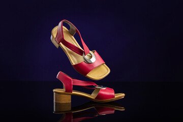 Pair of red leather women&rsquo;s sandals on dark blue background. Product photography and shopping concept