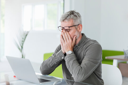 Exhausted businessman rubbing eyes at desk