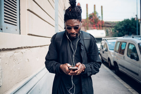 Young man with in-ear headphones using mobile phone on footpath