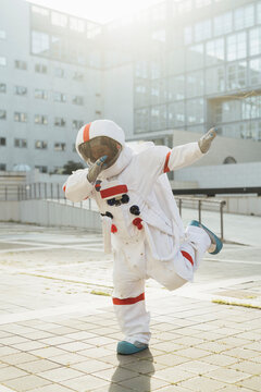 Young female astronaut doing dab on footpath outside building during sunny day