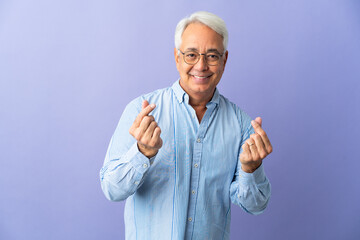 Naklejka premium Middle age Brazilian man isolated on purple background making money gesture