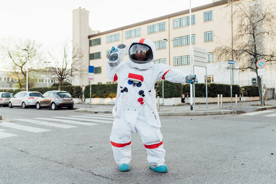 Young female astronaut listening music through boombox while standing on road in city