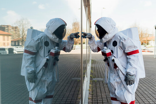 Male astronaut in space suit touching glass wall in city
