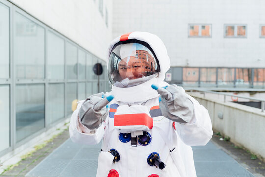 Young female astronaut showing middle finger while standing near building