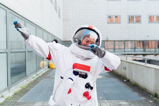 Female astronaut in space suit doing dab while standing near building
