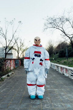 Young female astronaut wearing alien mask while standing on footpath