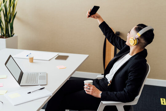 Businesswoman with headphones taking selfie through mobile phone in office