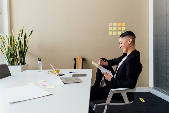 Smiling businesswoman writing on paper while sitting at desk in office