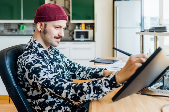 Man wearing knit hat using graphics tablet at home