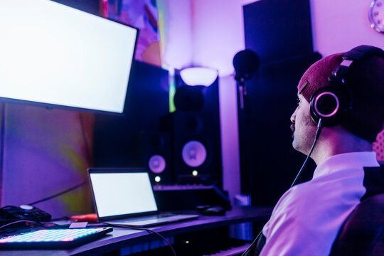Man wearing knit hat looking at device screen while listening music at studio