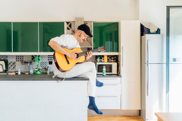Male composer with eyes closed playing guitar on kitchen island at home