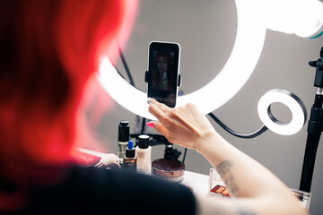 Female vlogger using mobile phone connected at ring light in studio
