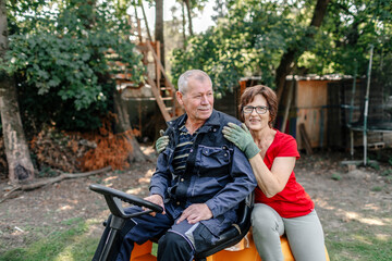 Smiling senior couple sitting on lawn mover in backyard