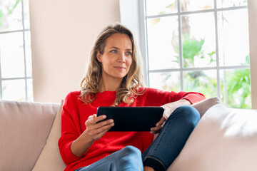 Smiling woman relaxing while holding digital tablet on couch in living room