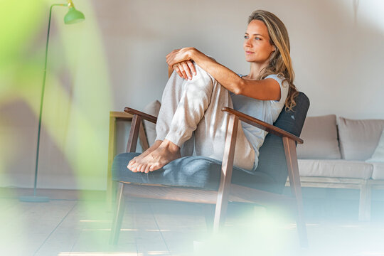 Thoughtful woman looking away while sitting on armchair at home