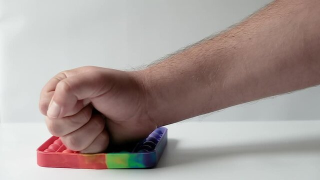Male hand on a white background beats a fist on a toy pop it checking strength or showing hatred