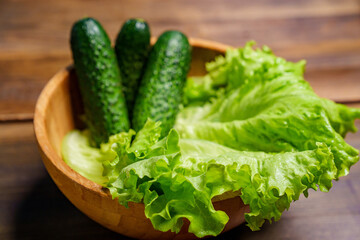lettuce and cucumbers in a bowl on a wooden cutting board on the table.