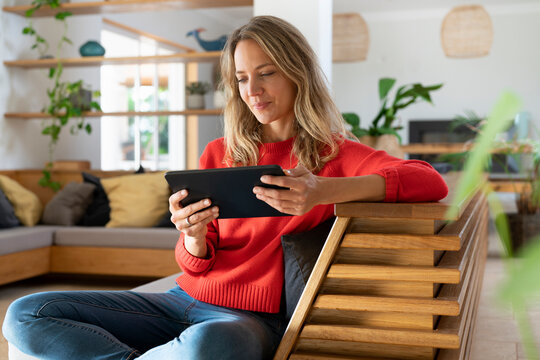 Woman using digital tablet while sitting on couch in living room