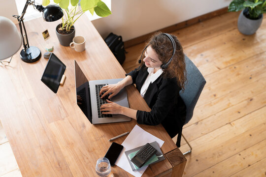 Female customer service representative with headphones speaking to client while working at laptop in home office