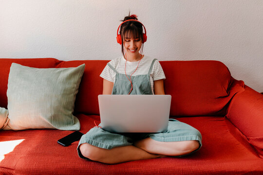Woman with headphones working on laptop in living room