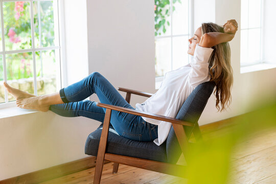 Relaxed woman with arms raised sitting on chair at home