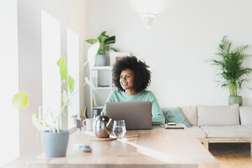 Smiling woman with laptop looking away at home