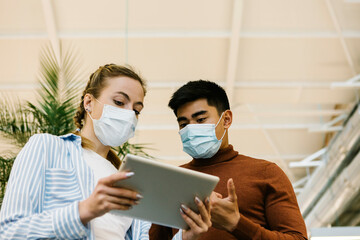 Young male and female entrepreneurs discussing over digital tablet at office during COVID-19
