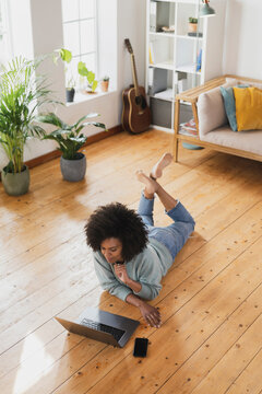 Young woman using laptop while lying on floor in living room