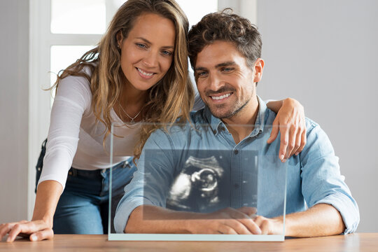 Happy couple looking at ultrasound image over transparent screen at home