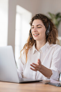 Contented female customer service representative with headphones explaining to client headphones at desk in home office