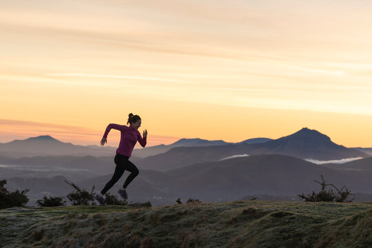 Female runner running on hill by dramatic sky