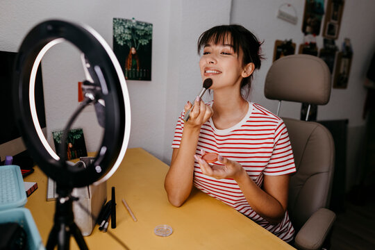 Female influencer using mobile phone while vlogging about make-up at studio