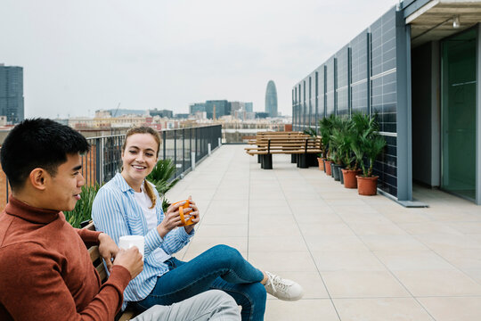 Smiling male and female professionals talking while having coffee at rooftop