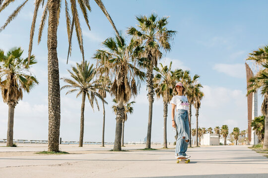 Mid adult woman skating by palm tree on footpath