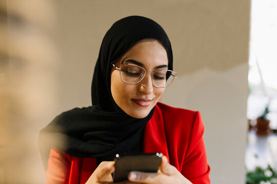 Woman wearing hijab smiling while using mobile phone in coffee shop